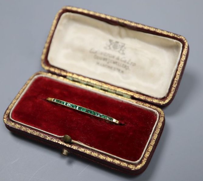 A yellow metal and graduated eighteen stone emerald set bar brooch, 36mm, gross 1.9 grams.